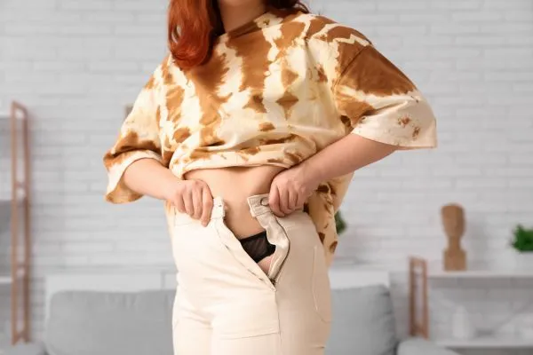 Image of woman trying to do her trousers up after pregnancy weight gain Chatham